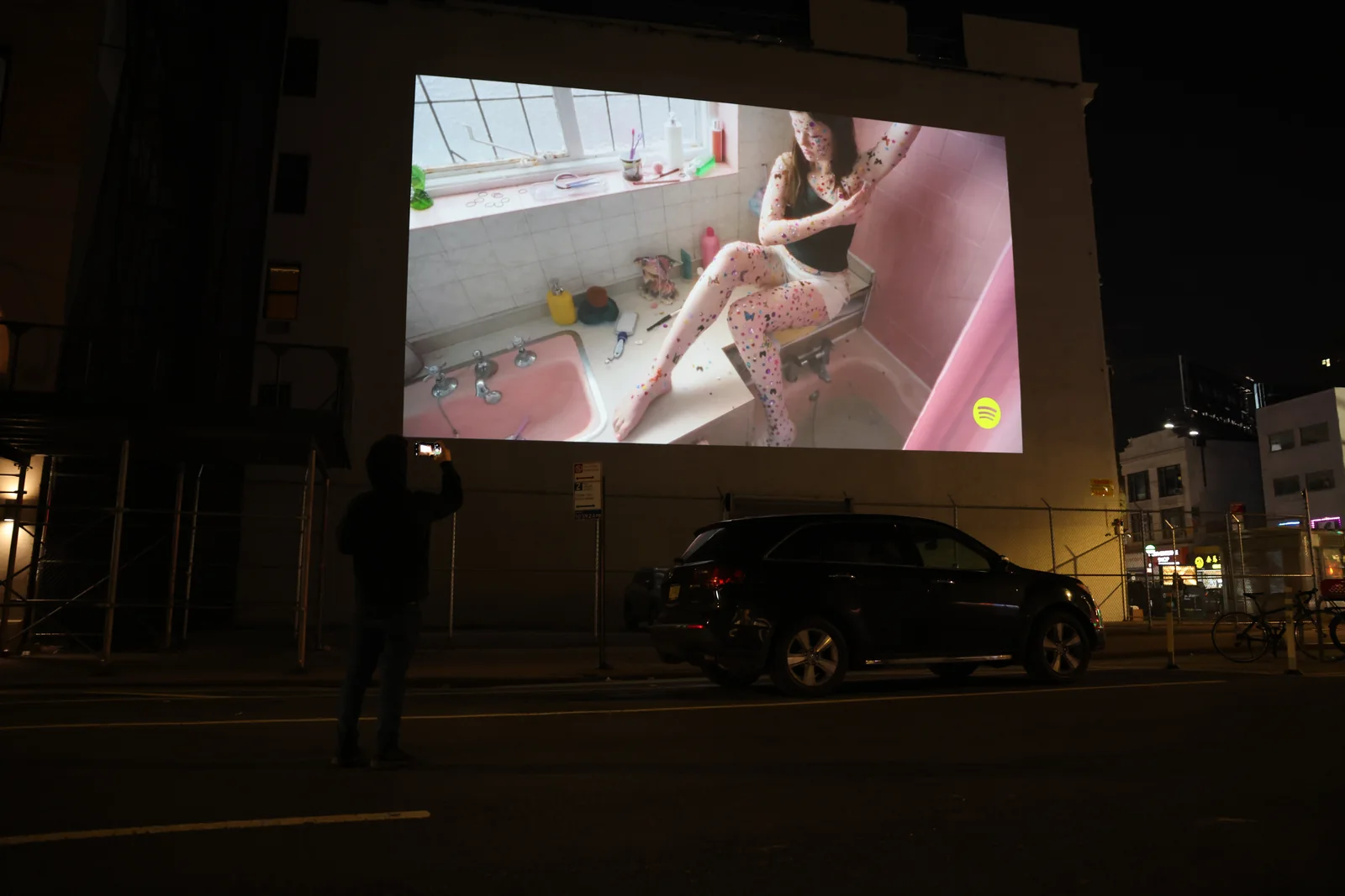 Projection advertising shown on a wall with a passerby recording it
